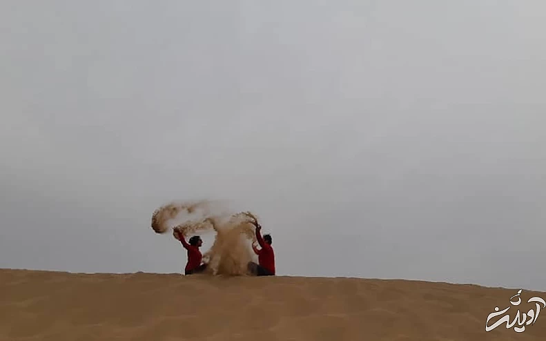 دو گردشگر روی تپه ای شنی در حال پاشیدن شن به هم